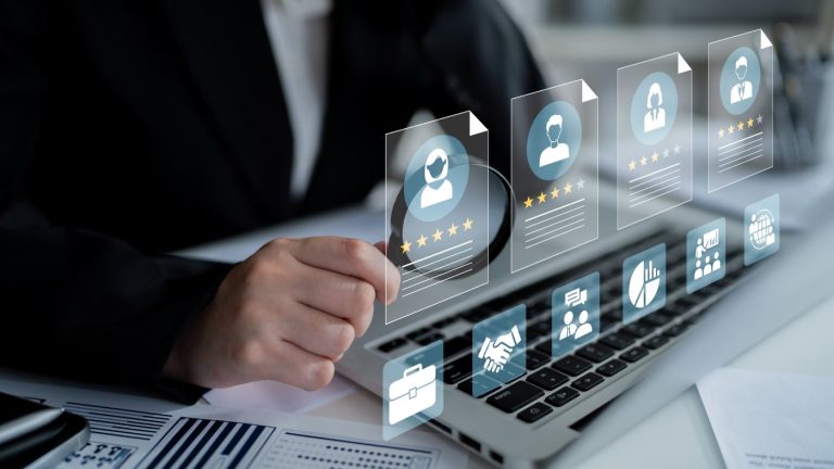 Unternehmensnachfolge Hausverwaltung: Eine Person nutzt eine Lupe auf einem Laptop mit eingeblendeten digitalen Nutzer-Icons, um die Strukturierung des Teams und der Kundenkontakte zu analysieren.